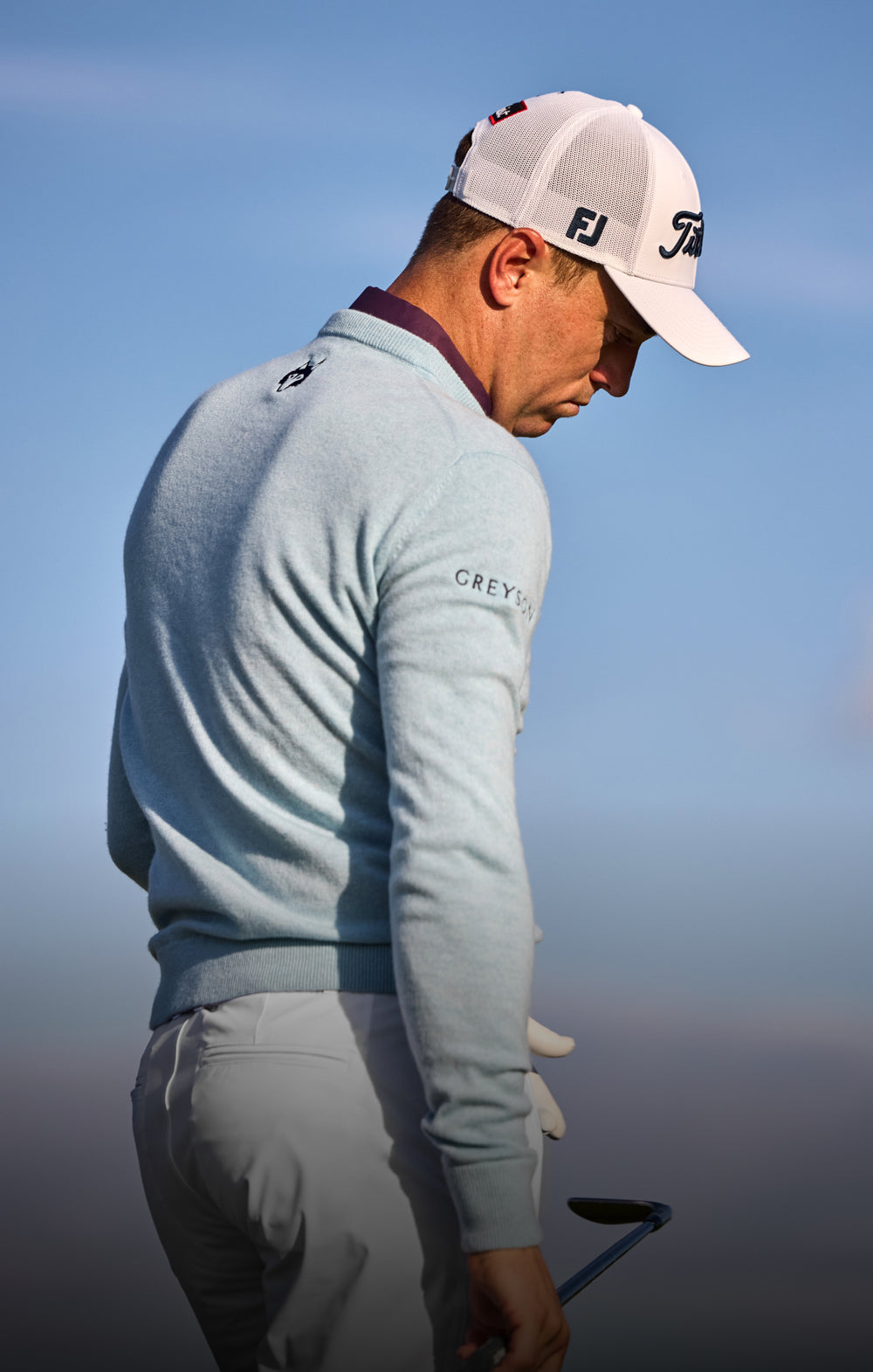a man on a golf course in a light blue sweater and white hat