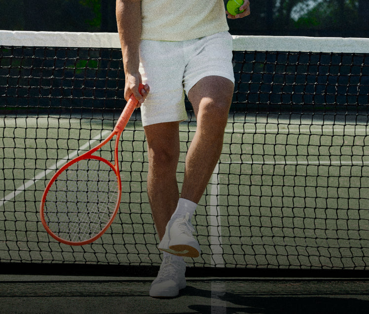 Person on a tennis court holding a racket and ball, standing behind the net.